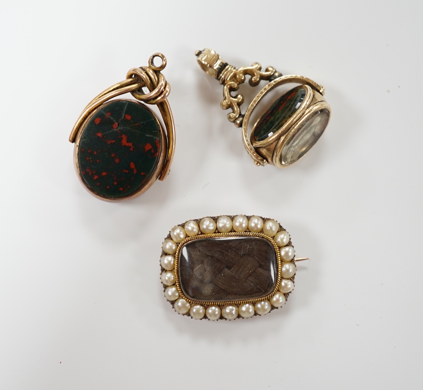 An early Victorian yellow metal and seed pearl set mourning brooch, with plaited hair, 23mm, together with two chalcedony set fob seals, including 9ct gold mounted.
